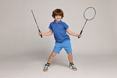 Little boy with badminton rackets on light grey background