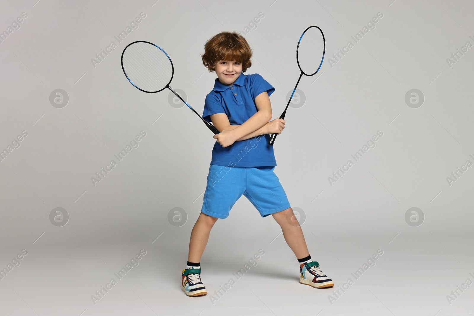 Photo of Little boy with badminton rackets on light grey background