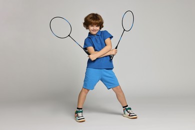 Photo of Little boy with badminton rackets on light grey background