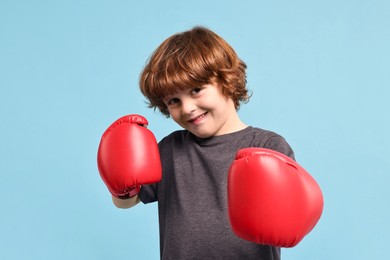 Photo of Little boy with boxing gloves on light blue background