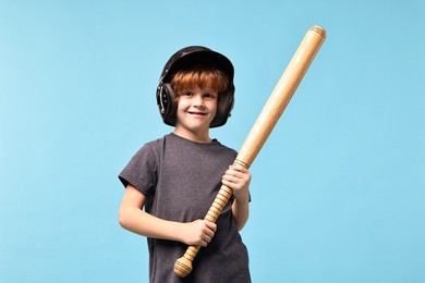 Little boy in helmet with baseball bat on light blue background