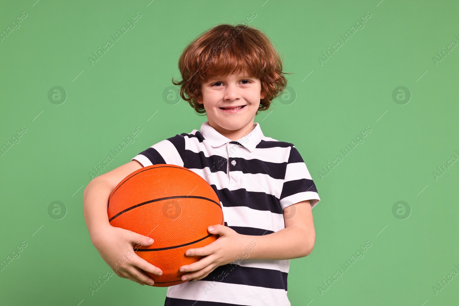 Photo of Little boy with basketball ball on light green background