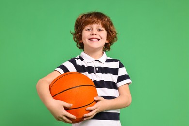 Little boy with basketball ball on light green background