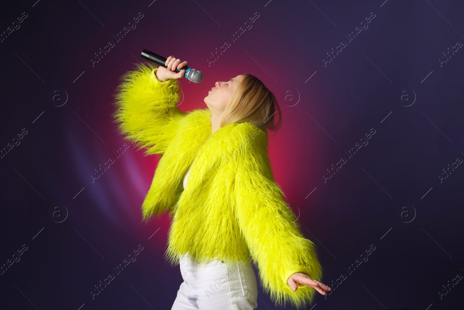 Photo of Talented singer in faux fur performing on dark background with pink light