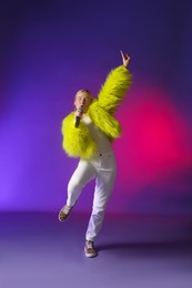 Photo of Talented singer in faux fur performing on purple background with pink light