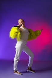 Photo of Talented singer in faux fur performing on purple background with pink light