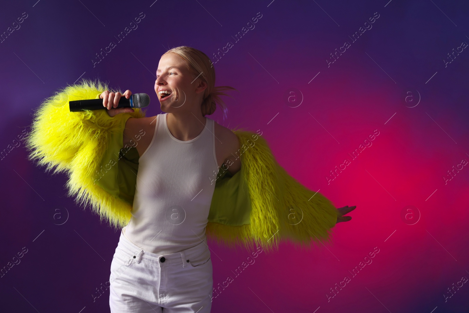 Photo of Talented singer in faux fur performing on purple background with pink light