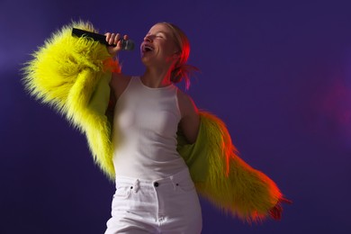 Photo of Talented singer in bright faux fur coat performing on purple background. Space for text