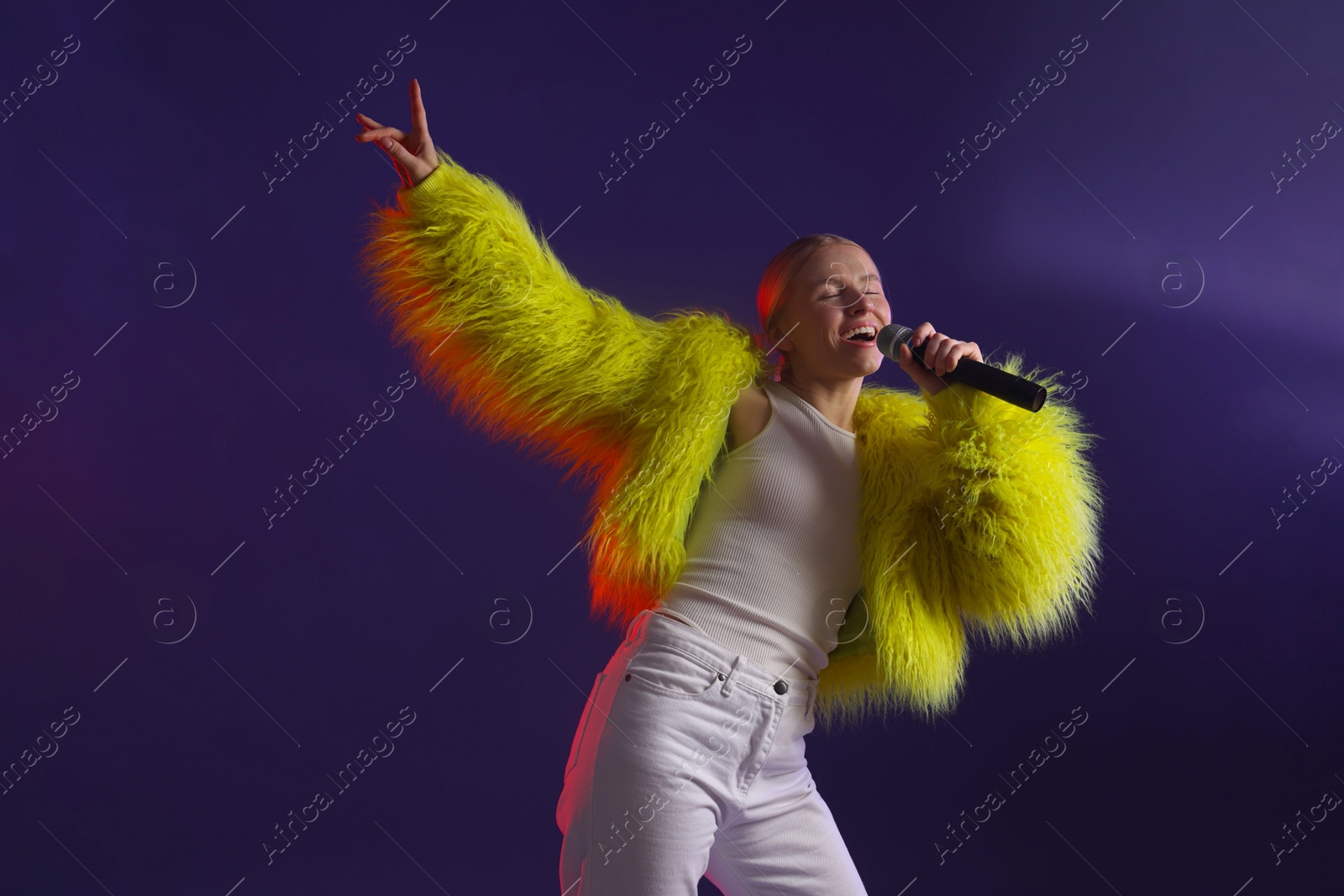 Photo of Talented singer in bright faux fur coat performing on purple background