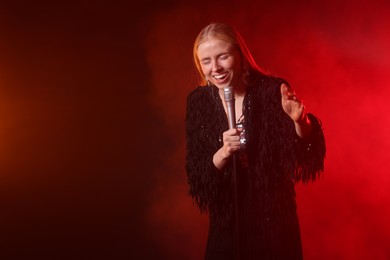 Photo of Beautiful singer performing on dark background with red light and smoke. Space for text