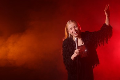 Photo of Beautiful singer performing on dark background with red light and smoke. Space for text