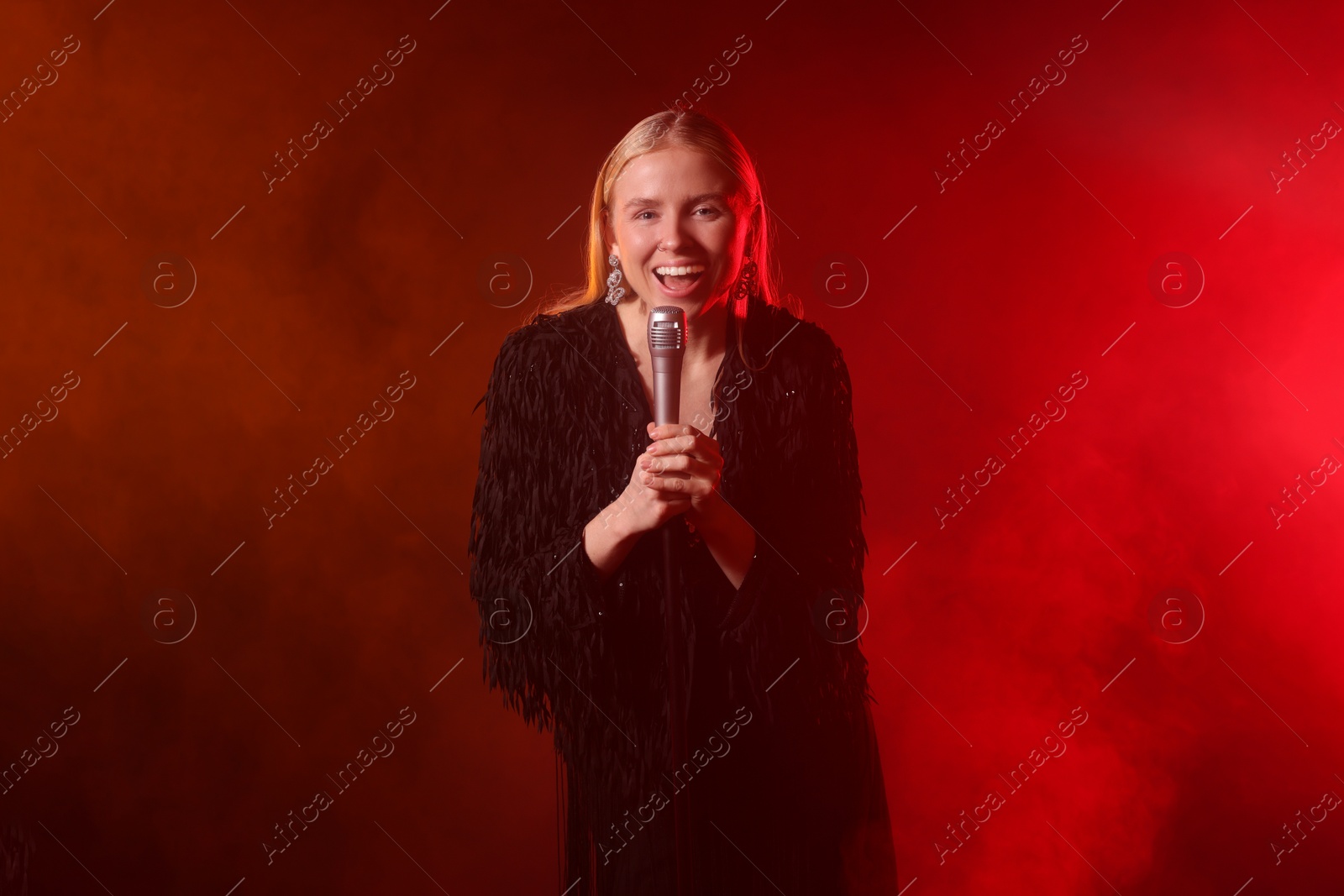 Photo of Beautiful singer performing on dark background with red light and smoke