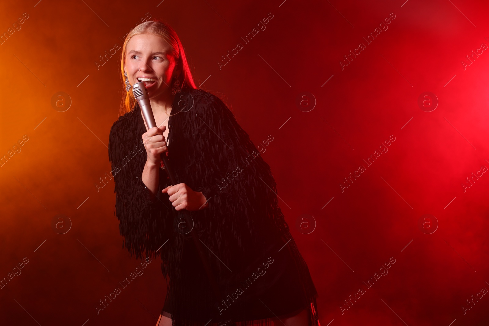 Photo of Beautiful singer performing on dark background with red light and smoke. Space for text