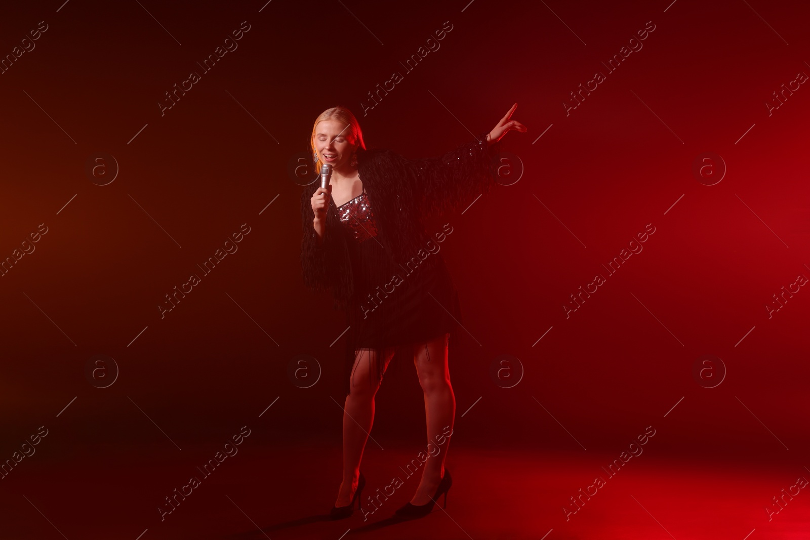 Photo of Beautiful singer performing on dark background with red light