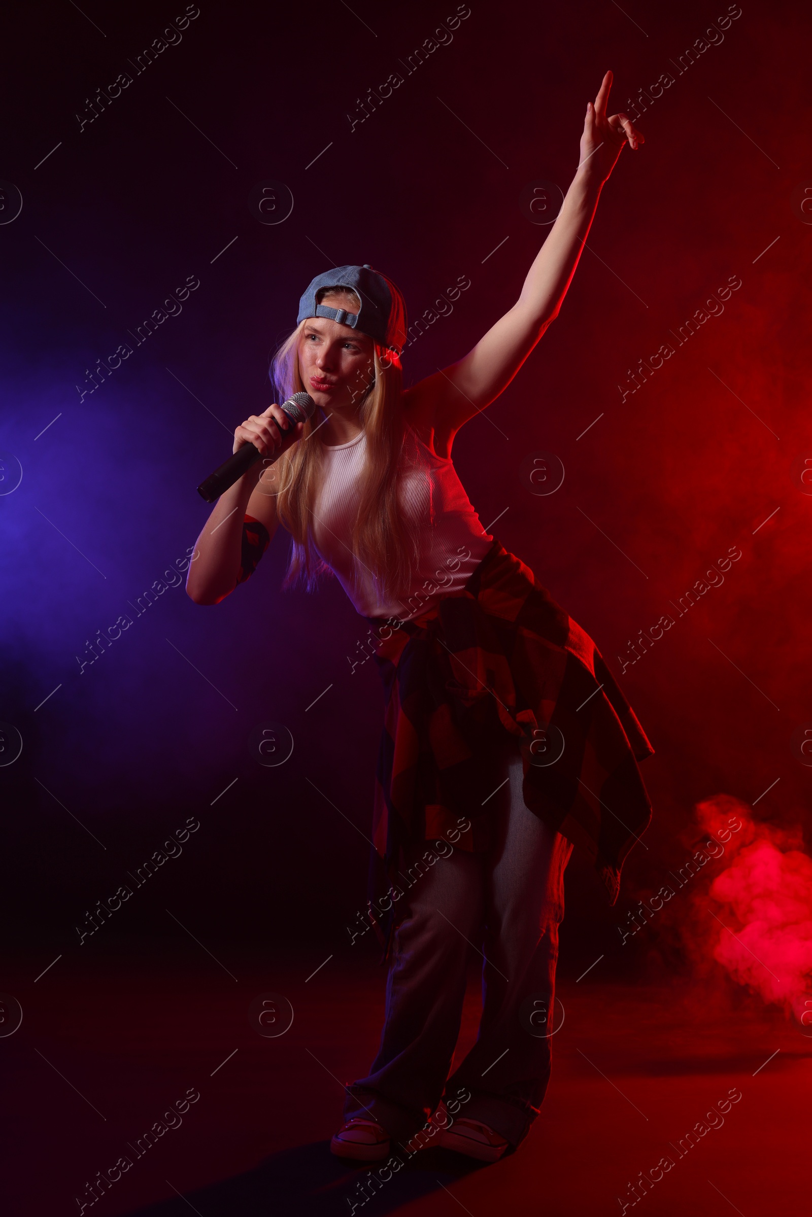 Photo of Talented singer performing on dark background with color lights and smoke