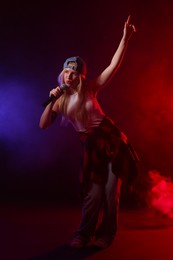 Photo of Talented singer performing on dark background with color lights and smoke