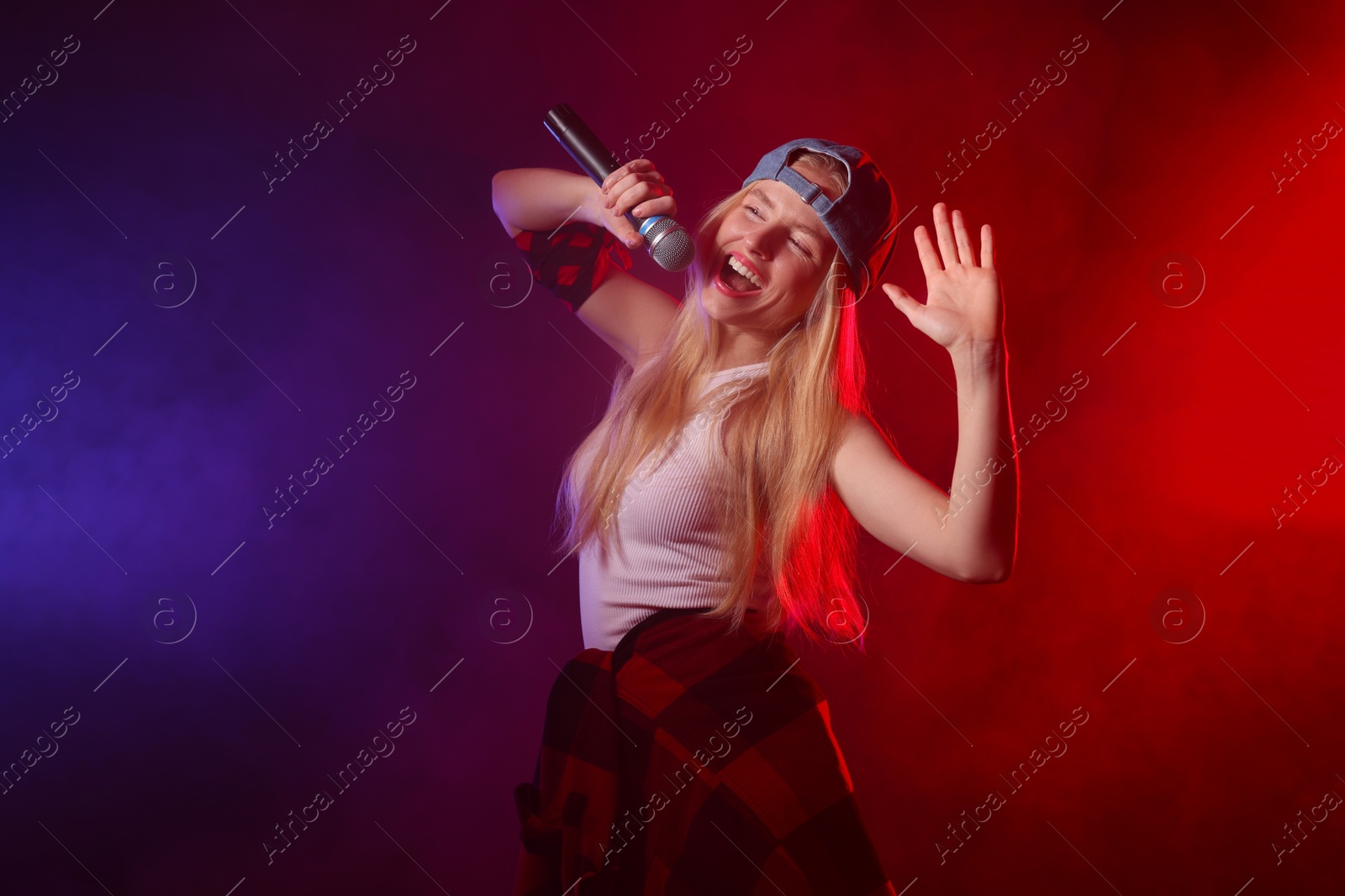 Photo of Talented singer performing on dark background with color lights and smoke