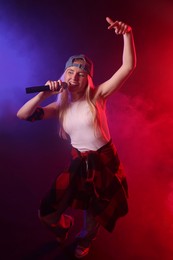 Photo of Talented singer performing on dark background with color lights and smoke