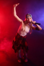 Photo of Talented singer performing on dark background with color lights and smoke