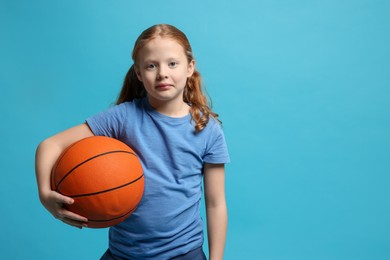 Little girl with basketball ball on light blue background, space for text