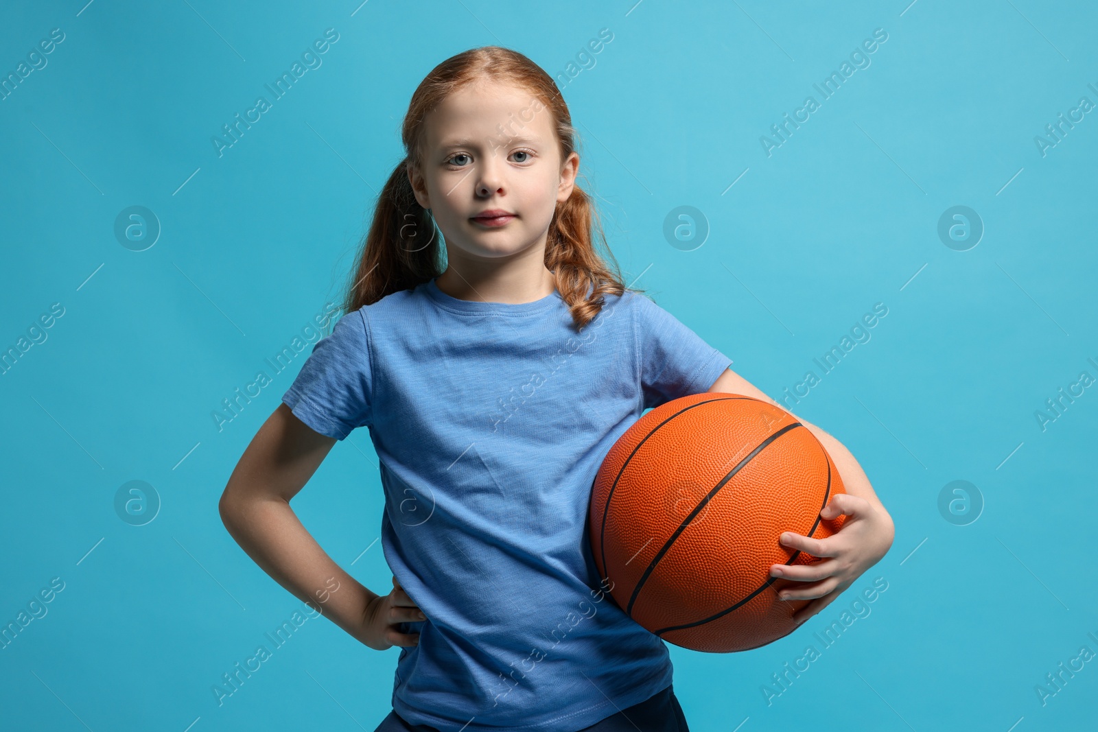 Photo of Little girl with basketball ball on light blue background