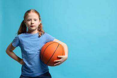 Photo of Little girl with basketball ball on light blue background, space for text