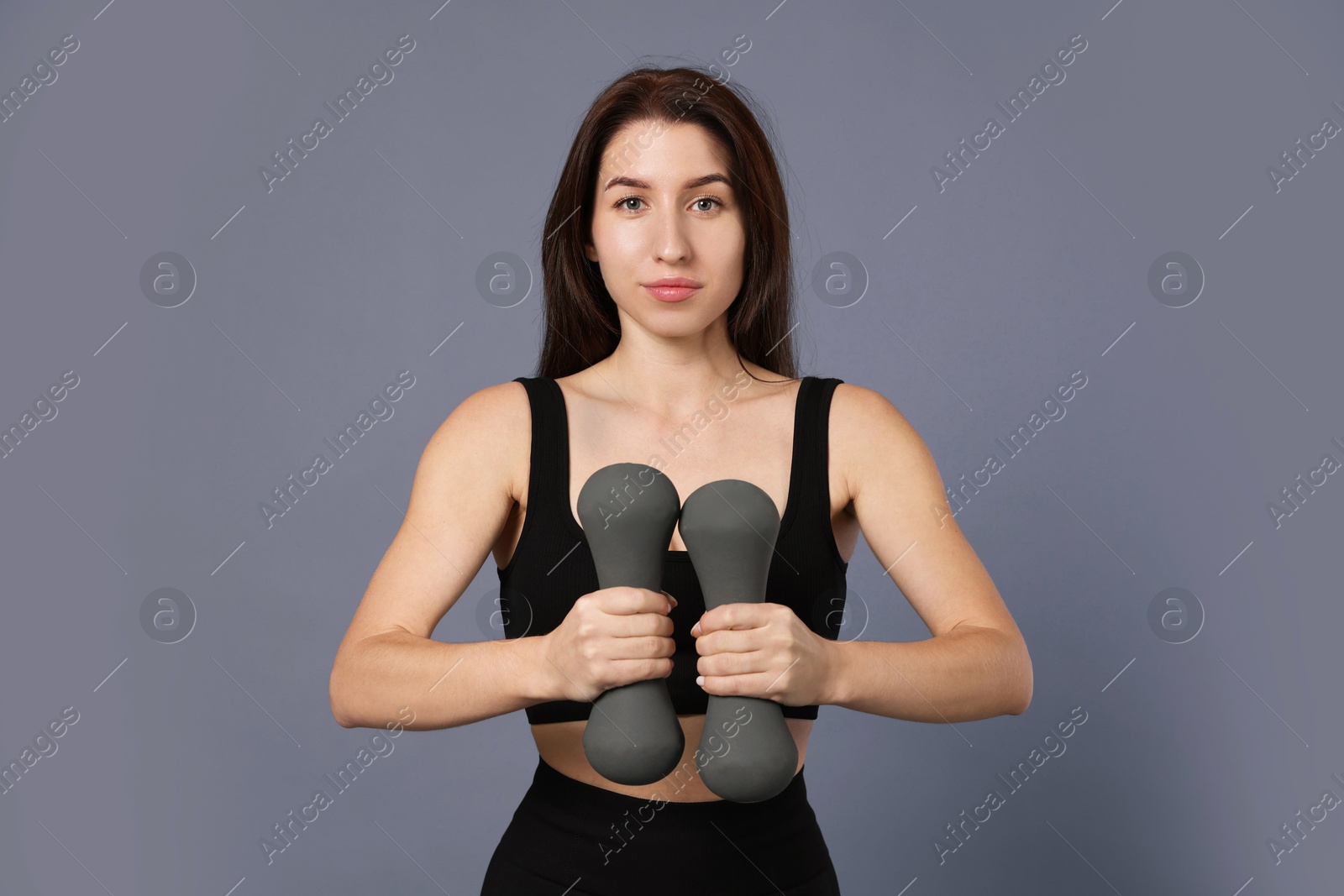 Photo of Woman in sportswear exercising with dumbbells on grey background