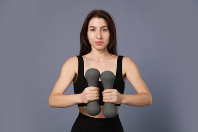 Photo of Woman in sportswear exercising with dumbbells on grey background