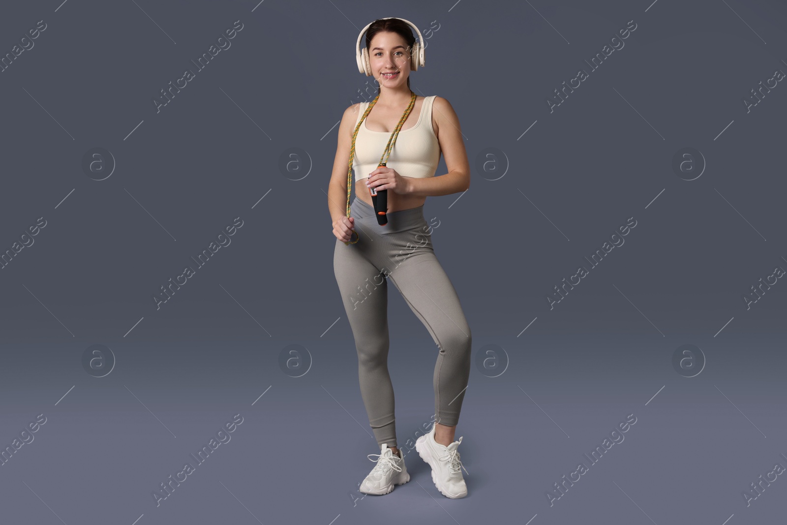 Photo of Woman in sportswear with headphones and skipping rope on grey background