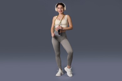 Photo of Woman in sportswear with headphones and skipping rope on grey background