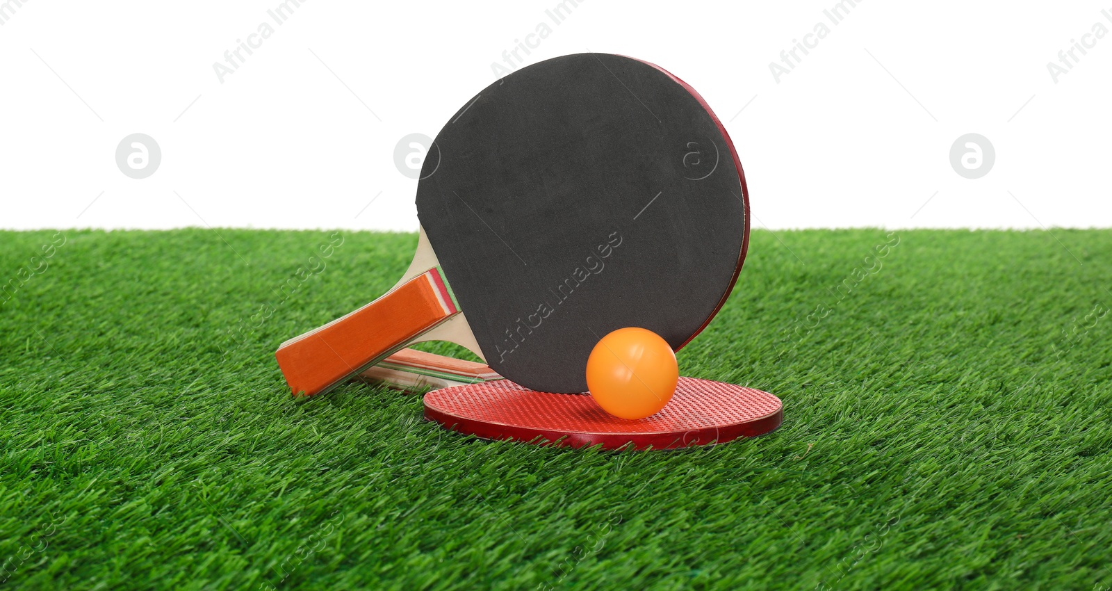 Photo of Ping pong rackets and ball on green grass against white background. Sport equipment