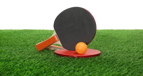 Ping pong rackets and ball on green grass against white background. Sport equipment