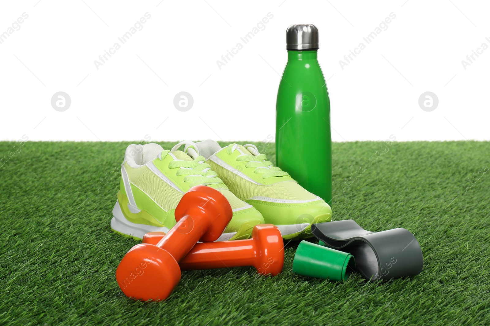 Photo of Dumbbells, elastic bands, thermo bottle and sneakers on green grass against white background. Sport equipment