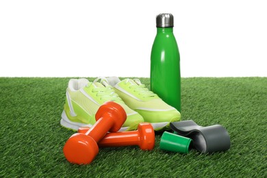 Photo of Dumbbells, elastic bands, thermo bottle and sneakers on green grass against white background. Sport equipment