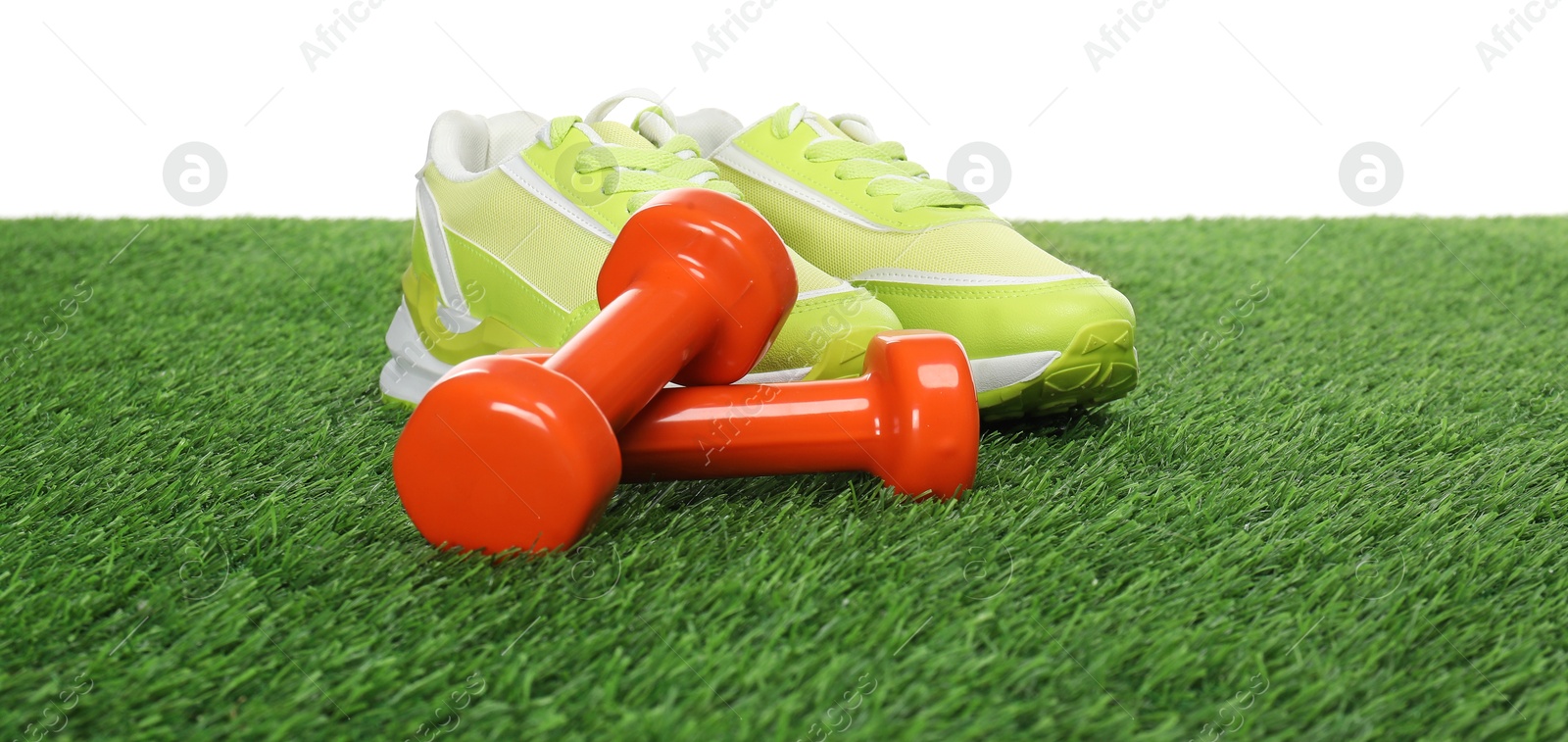 Photo of Dumbbells and sneakers on green grass against white background. Sport equipment