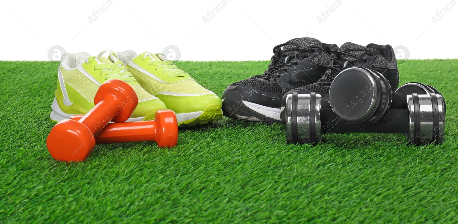 Photo of Dumbbells and sneakers on green grass against white background. Sport equipment