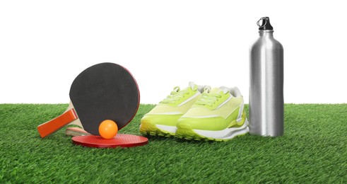 Photo of Ping pong rackets, ball, thermo bottle and sneakers on green grass against white background. Sport equipment