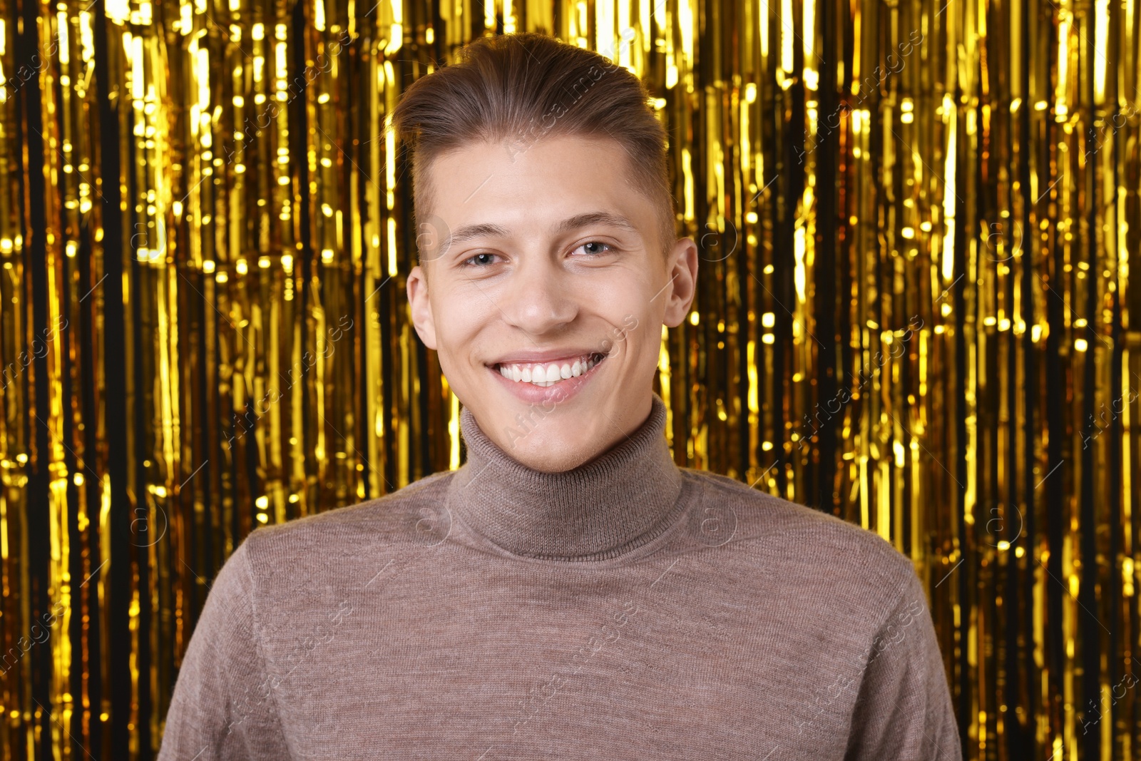 Photo of Happy young man against golden foil curtain