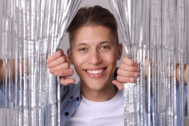 Photo of Happy young man looking out through silver foil curtain against light background