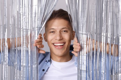 Photo of Happy young man looking out through silver foil curtain against light background