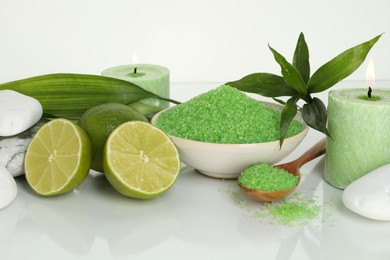 Photo of Spa composition with fresh limes, sea salt, massage stones and bamboo leaves on mirror surface against white background, closeup