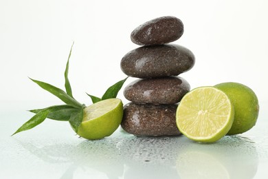 Photo of Spa composition with fresh limes, stack of pebble stones and bamboo leaves on wet mirror surface against white background