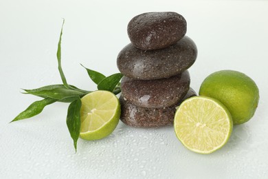 Photo of Spa composition with fresh limes, stack of pebble stones and bamboo leaves on wet surface