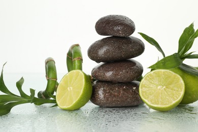 Photo of Spa composition with fresh limes, stack of pebble stones and bamboo leaves on wet mirror surface against white background, closeup