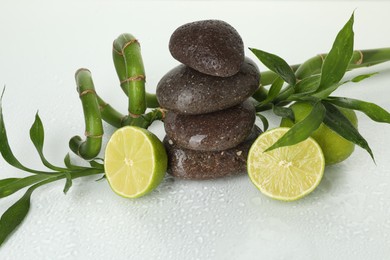 Photo of Spa composition with fresh limes, stack of pebble stones and bamboo on wet surface, closeup