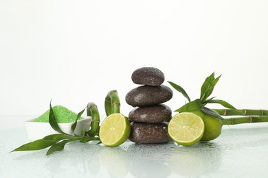 Photo of Spa composition with fresh limes, sea salt, massage stones and bamboo on wet mirror surface against white background