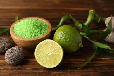 Photo of Spa composition with fresh limes, sea salt, stones and bamboo on wooden table, closeup