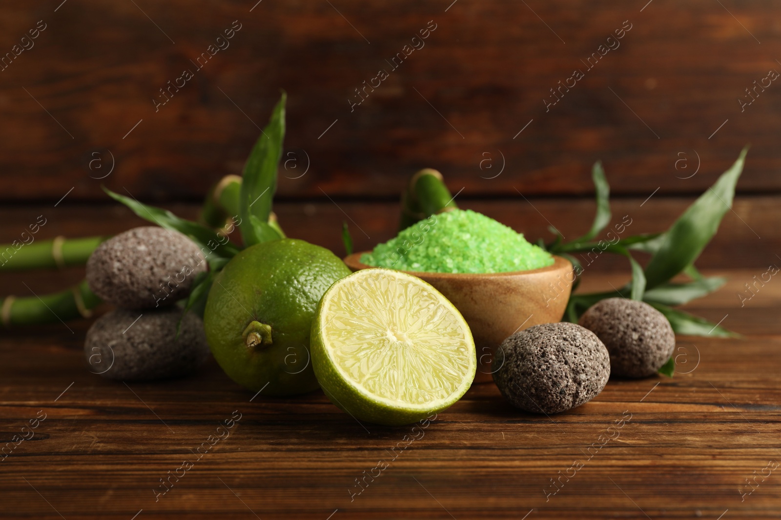 Photo of Spa composition with fresh limes, sea salt, stones and bamboo leaves on wooden table, closeup