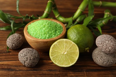 Photo of Spa composition with fresh limes, sea salt, stones and bamboo leaves on wooden table, closeup