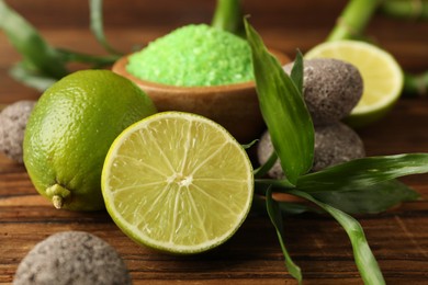 Photo of Spa composition with fresh limes, sea salt, stones and bamboo leaves on wooden table, closeup
